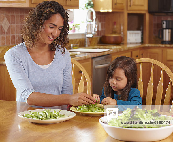 Mother and daughter shelling peas at dining table