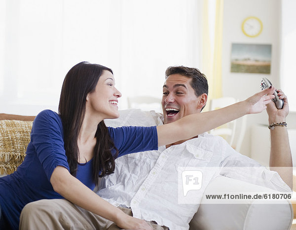 Laughing mixed race man keeping remote control away from wife