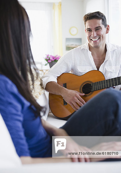 Mixed race man playing guitar for wife
