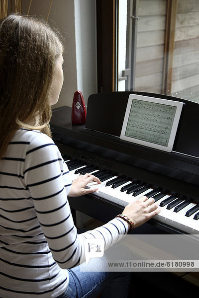 Mädchen spielt am Klavier  liest die Noten von einem iPad  Tablet-Computer ab