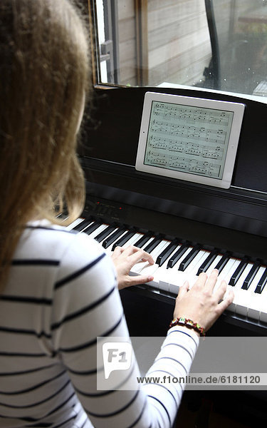 Girl playing the piano  reading the notes from an iPad  tablet computer