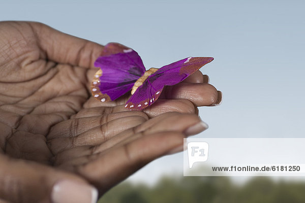 Black woman's hands holding purple butterfly