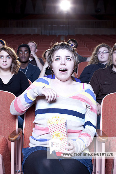 Surprised Caucasian woman eating popcorn in movie theater