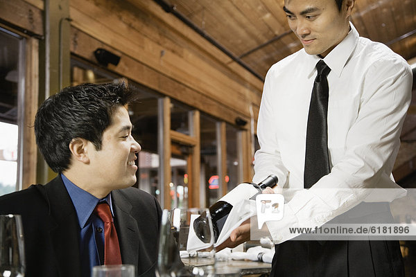 Asian waiter showing wine to customer