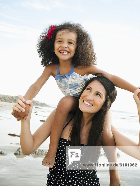 Hispanic mother carrying daughter on shoulders at beach