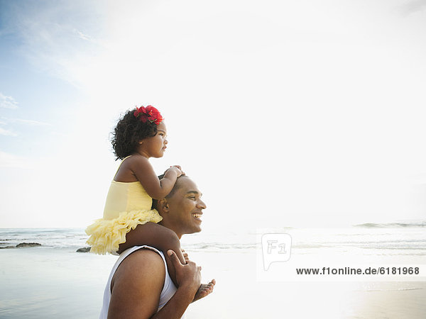 Black father carrying daughter on shoulders at beach