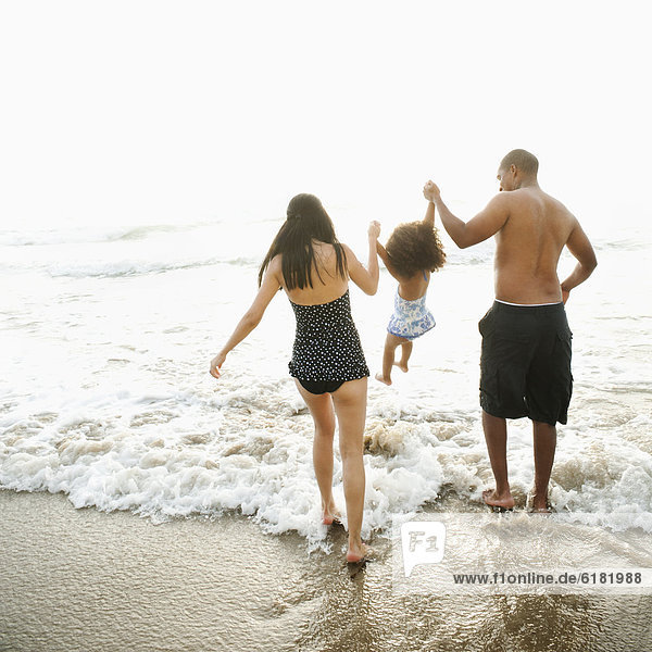 Parents swinging daughter between them on beach