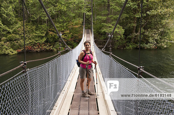 Hispanic woman hiking over bridge in woods