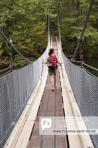 Hispanic woman hiking over bridge in woods