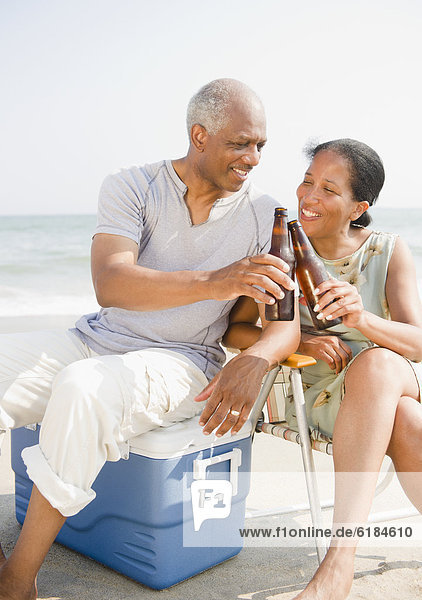 Black couple drinking beer on beach
