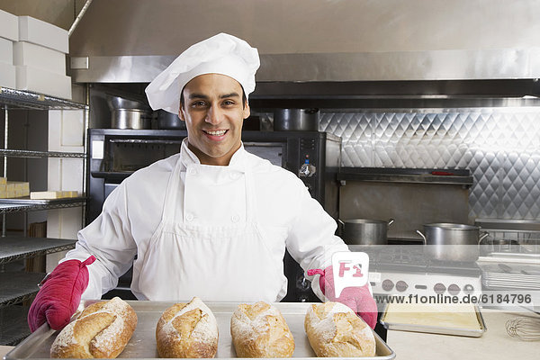Hispanic male baker holding tray of fresh bread