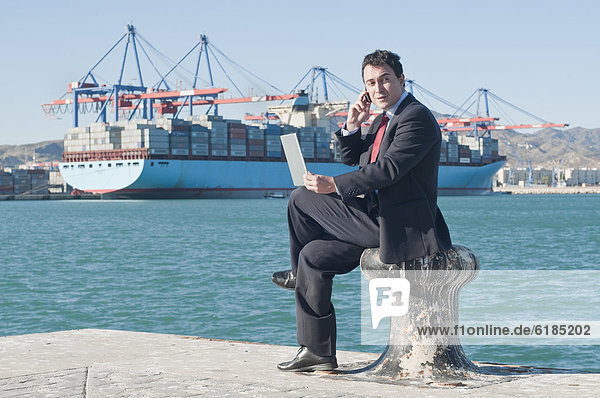 Hispanic businessman holding laptop with container ship in background
