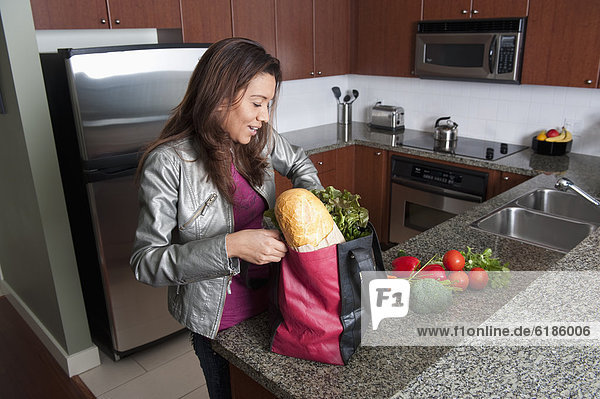 Hispanic woman unloading groceries in kitchen