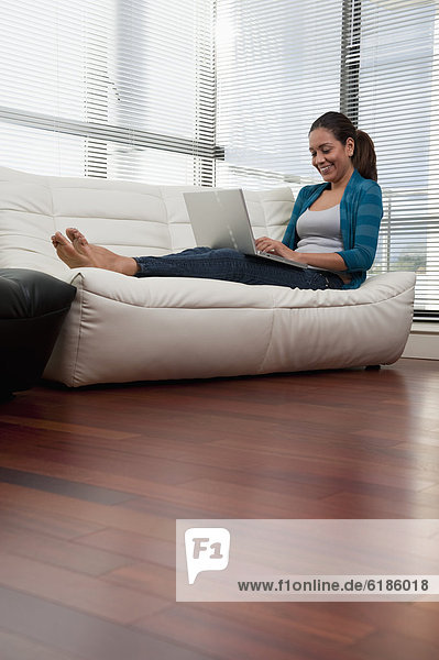Hispanic woman on sofa using laptop