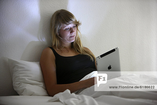 Junge Frau surft im Bett mit einem iPad Tablet-Computer per Drahtlosverbindung im Internet