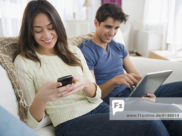 Couple using technology on sofa together