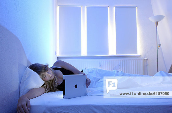 Junge Frau surft im Bett mit einem iPad Tablet-Computer per Drahtlosverbindung im Internet