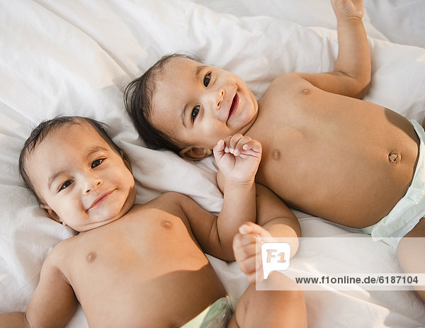 Mixed race twins in diapers laying on bed