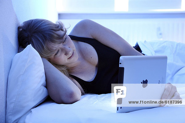 Junge Frau surft im Bett mit einem iPad Tablet-Computer per Drahtlosverbindung im Internet