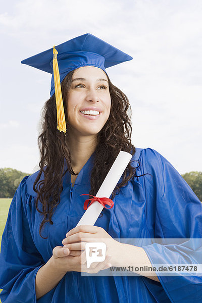 Mixed race woman wearing graduation cap and gown holding diploma