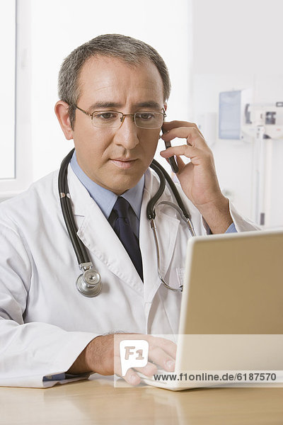 Hispanic doctor with laptop talking on cell phone
