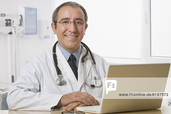 Hispanic doctor sitting at desk with laptop