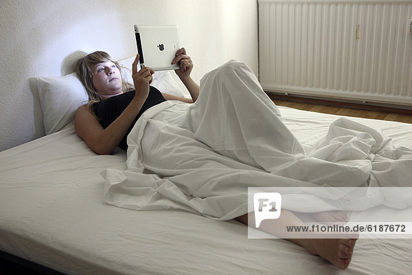 Junge Frau surft im Bett mit einem iPad  Tablet-Computer per Drahtlosverbindung im Internet