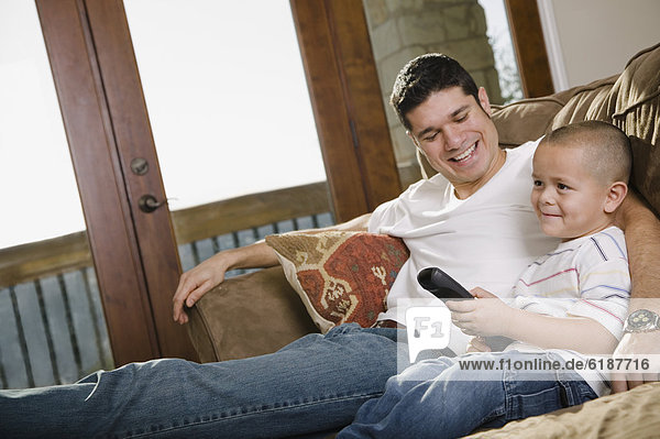Hispanic father and son watching television on sofa