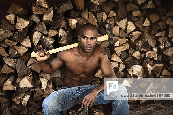 Bare chested African American man near woodpile holding ax