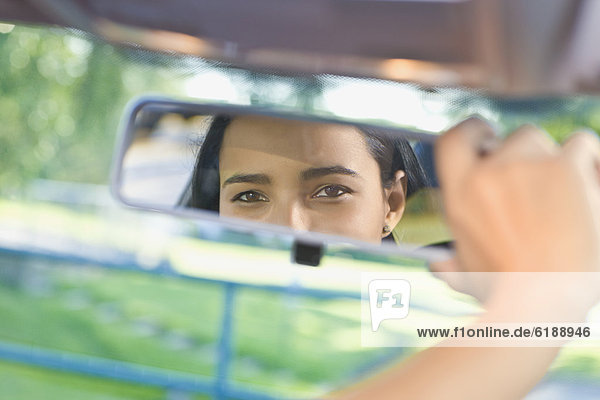 Hispanic woman adjusting rear view mirror in car
