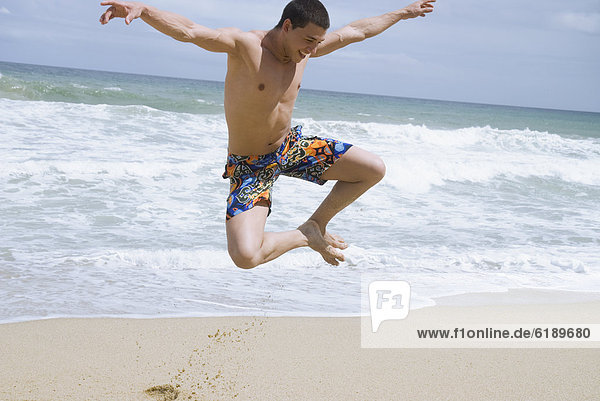 Hispanic man at beach jumping in mid-air