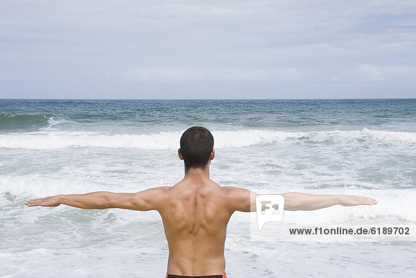 Hispanic man with arms out at beach