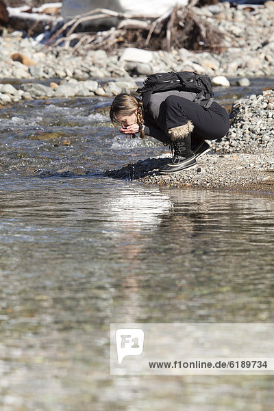Caucasian hiker drinking from remote stream