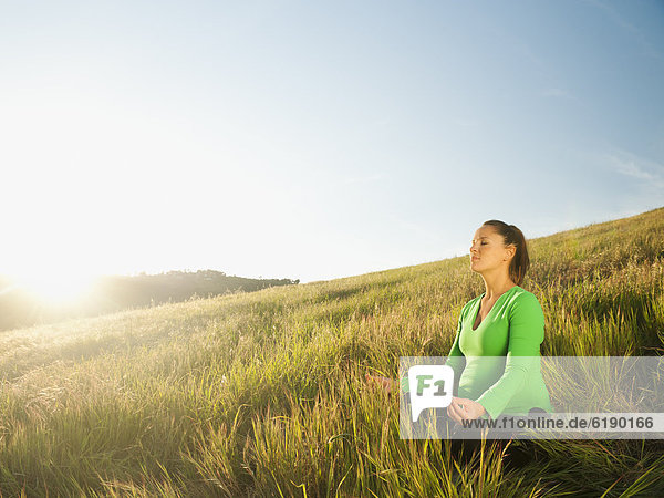 Pregnant Hispanic woman practicing yoga in field