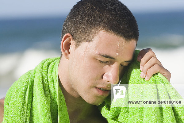 Sweating Hispanic man wiping face with towel