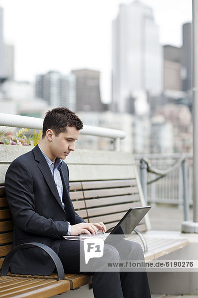 Mixed race businessman using laptop on city bench