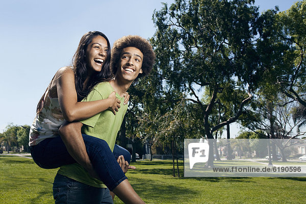 Teenager carrying girlfriend on his back in park