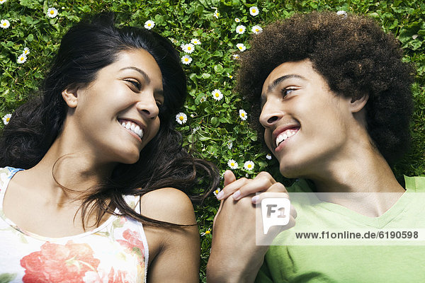 Teenage couple laying in grass holding hands