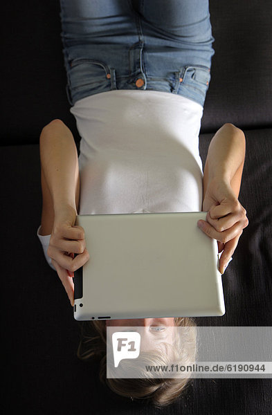Junge Frau liegt auf Sofa und surft drahtlos im Internet mit einem iPad Tablet-Computer