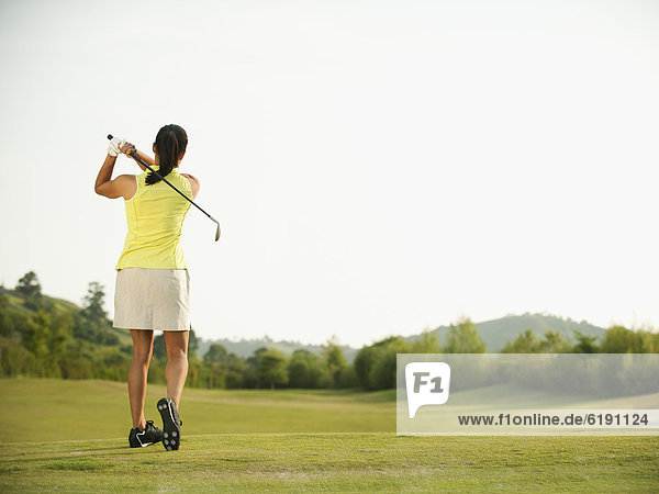Mixed race woman swinging golf club on golf course