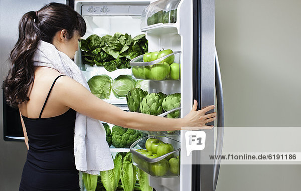 Mixed race woman looking at green vegetables in refrigerator