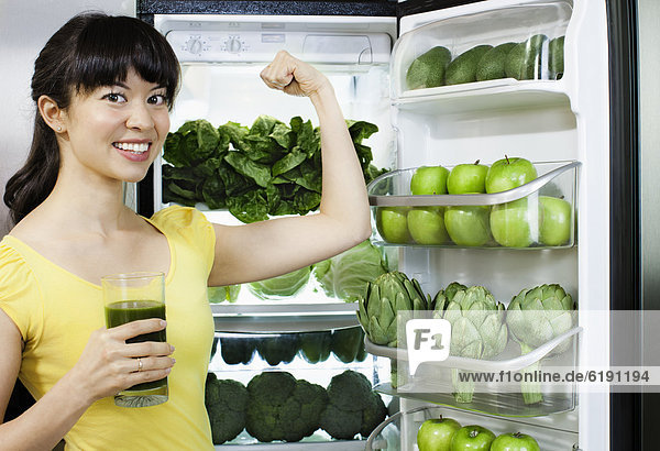 Mixed race woman drinking healthy drink near refrigerator