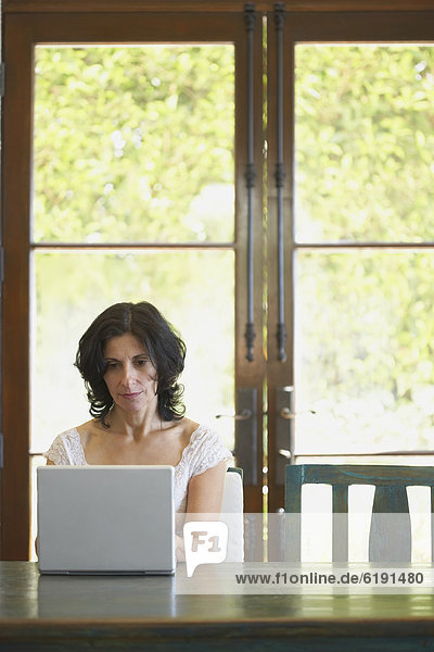 Confident Middle Eastern woman typing on laptop in dining room