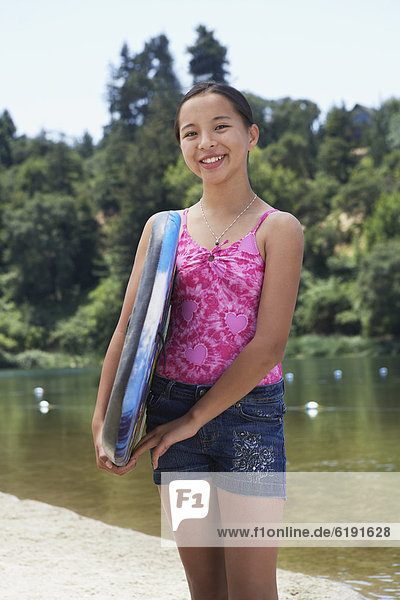 Mixed race girl holding boogie board near lake