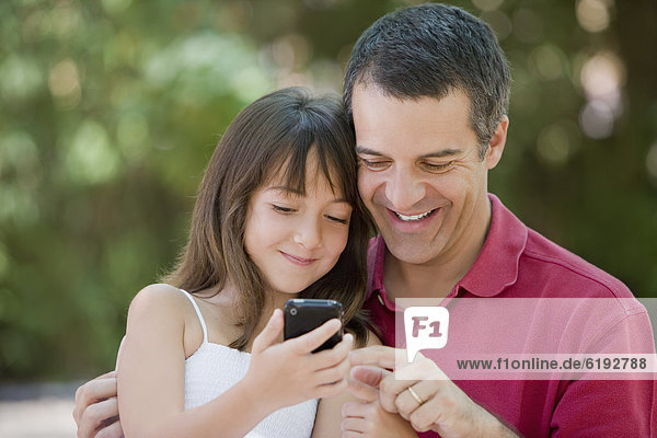 Hispanic father and daughter text messaging on cell phone