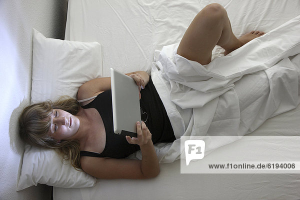 Junge Frau im Bett surft mit einem iPad Tablet-Computer per Drahtlosverbindung im Internet