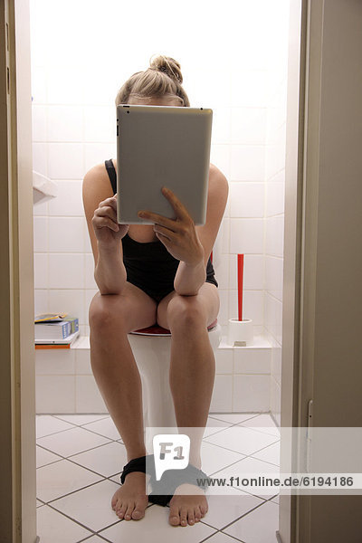 Junge Frau auf der Toilette surft mit einem iPad Tablet-Computer per Drahtlosverbindung im Internet