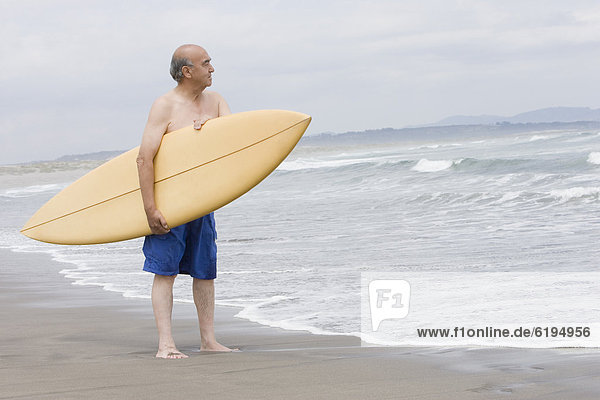 Senior Hispanic man holding surfboard on beach