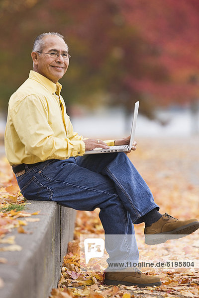 Hispanic man using laptop outdoors in autumn