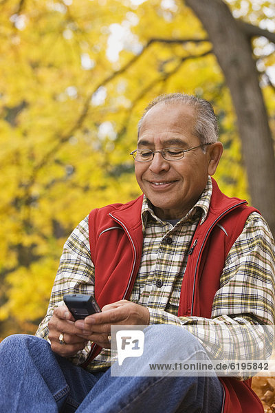 Hispanic man using cell phone outdoors in autumn